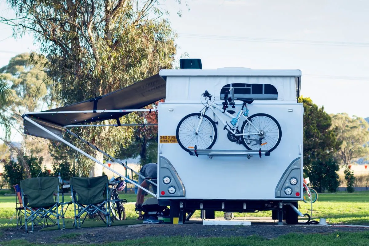 En campingvogn på en plads med udslået markise og to cykler på en holder monteret bagpå