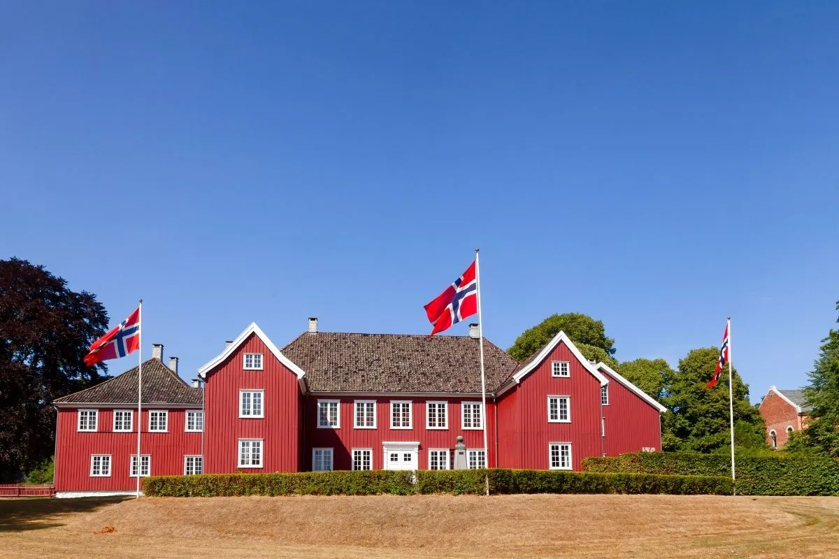 Herregården in Larvik, a long red-painted wooden manor house with white window frames and Norwegian flags flying in front